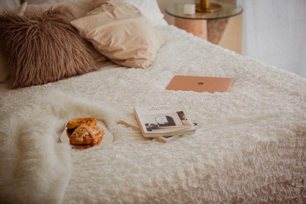 pastries-and-magazines-sit-on-bed-next-to-gold-macbook